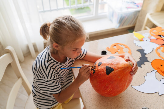 A girl paints a pumpkin with paints for Halloween.