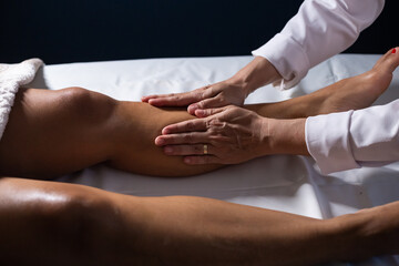 Um profissional fazendo massagem terapeutica nas pernas do paciente que está deitado em uma maca. - obrazy, fototapety, plakaty