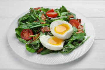 Delicious salad with boiled egg, bacon and tomatoes on white wooden table, closeup