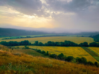 Fototapeta na wymiar Morning fog over the fields in the valley. A plain under gentle hills. Dawn landscape.