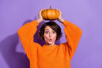 Photo of young pretty girl astonished playful grow big fresh pumpkin isolated over purple color background