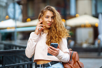 Fototapeta premium Beautiful woman with phone while walking in the street. Happy woman typing sms on smartphone in city. Lifestyle, travel, tourism, nature.