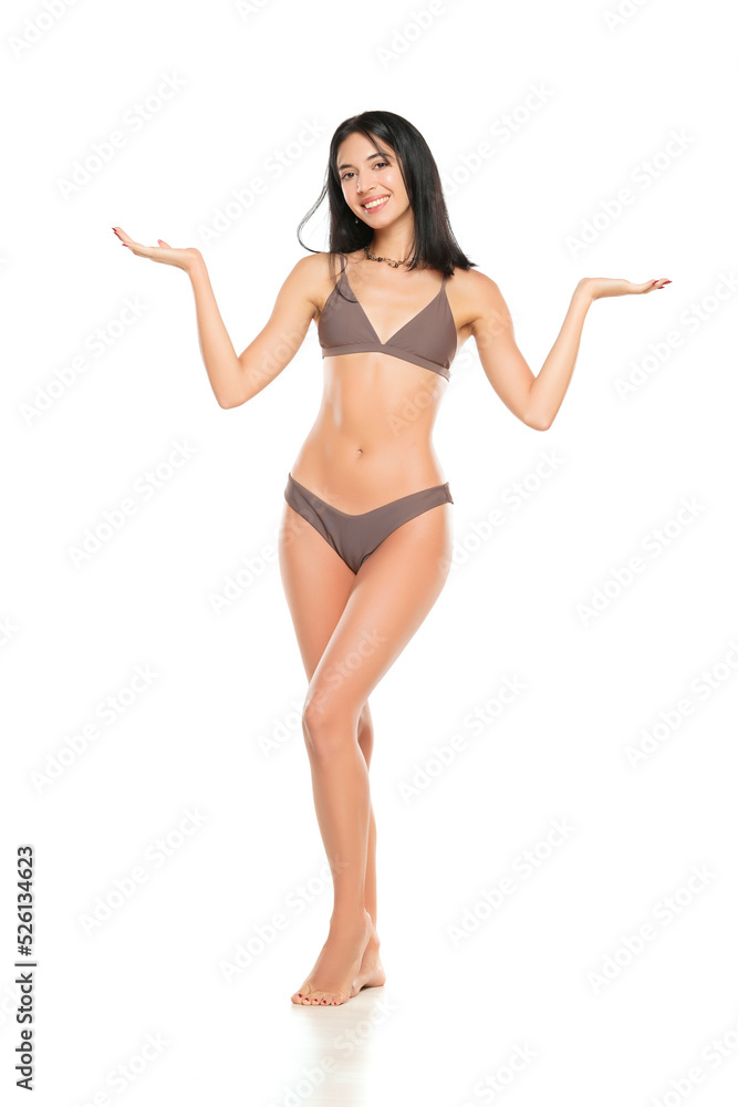 Wall mural young smiling brunette woman in bikini swimsuit advertising imaginary object on her hand on a white 