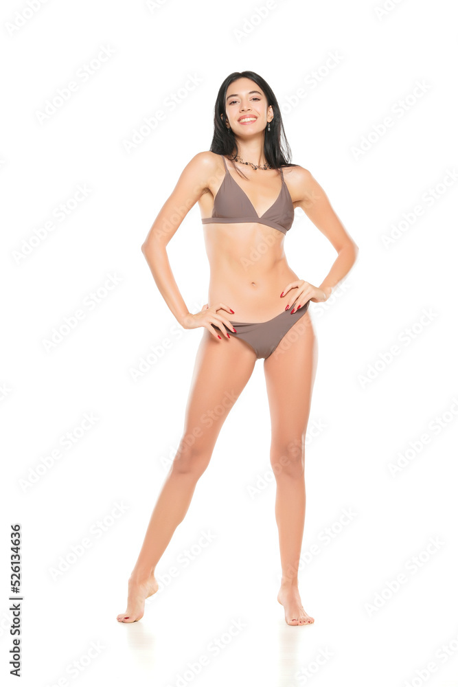 Wall mural young smiling brunette woman in bikini swimsuit posing on a white background.