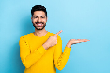 Photo of cute cheerful guy dressed yellow pullover pointing holding arm empty space isolated blue color background