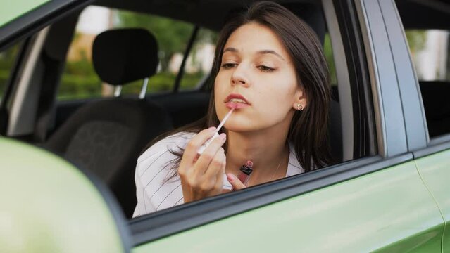 Young woman sit in car during travelling break. Slow motion of girl applying lipstick on lips. Cosmetics time and face care. Make up routine.