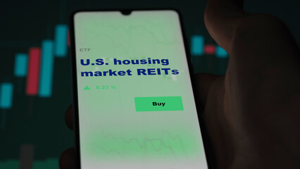 An investor's analyzing the real estate investment trusts  u.s., u.s.a.reit on screen. A phone shows the ETF's prices U.S. housing market REITs