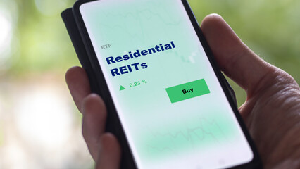 An investor's analyzing the real estate investment trusts fund reit on screen. A phone shows the ETF's prices residential REITs