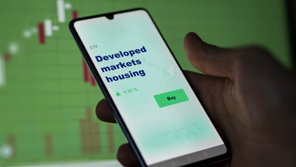 An investor's analyzing the DMEC on screen. A phone shows the ETF's prices developed markets housing