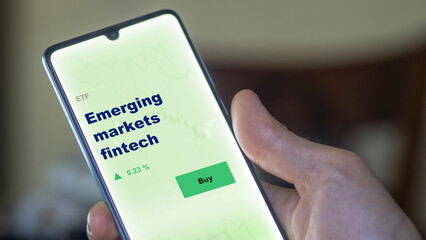 An investor's analyzing the  etf fund on screen. A phone shows the ETF's prices emerging markets fintech to invest