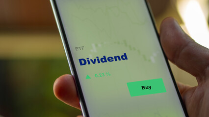 An investor's analyzing the dividend etf fund on screen. A phone shows the ETF's prices stocks to invest