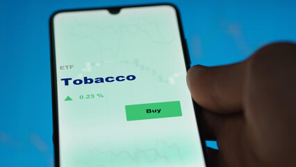 An investor's analyzing the tobacco etf fund on screen. A phone shows the ETF's prices stocks to invest