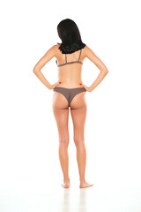 Fototapeta premium Back view of a young brunette woman in bikini swimsuit posing on a white background.