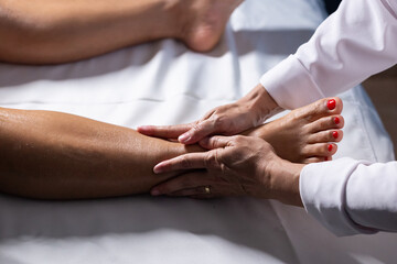 Um profissional fazendo massagem terapêutica no joelho do paciente que está deitado na maca. - obrazy, fototapety, plakaty
