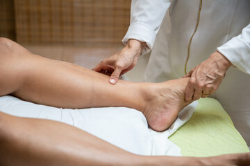 Um profissional fazendo massagem terapeutica na perna do paciente que está deitado na maca. - obrazy, fototapety, plakaty