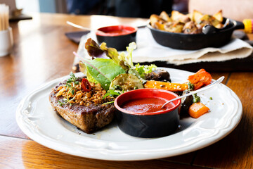 Pork steak with ketchup and salad on a white plate on a table in a restaurant.