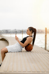 Fototapeta na wymiar Woman basketball player using smartphone apps and listening to music. Moment of leisure and rest