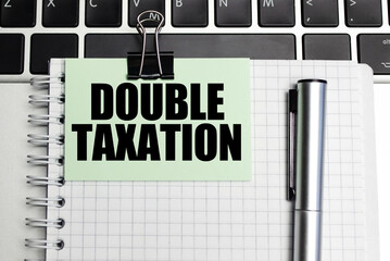 DOUBLE TAXATION words on green sticker and pen on laptop