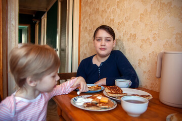 Toddler girl with older sister at   breakfast table eating pancakes.