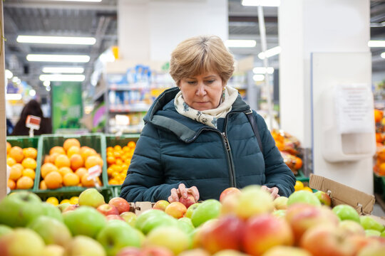 Smiling senior woman picking apple at the grocery shop