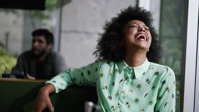Joyful African American woman sitting at coffee shop laughing out loud