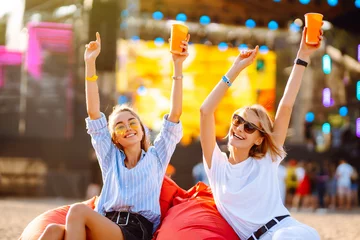 Fotobehang Two young woman  having a great time at a music festival. Happy girlfriends rinking beer and having fun at Beach party. Summer holiday, vacation concept. © maxbelchenko
