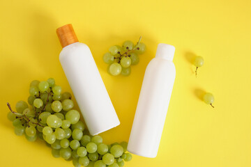 two mock up blank white bottles and grapes on yellow background