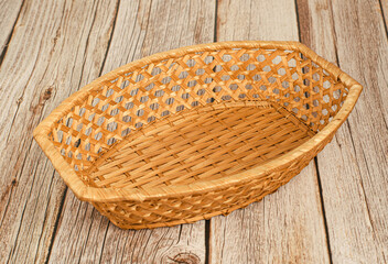 Small brown empty wicker basket for products on wooden background, texture, close-up