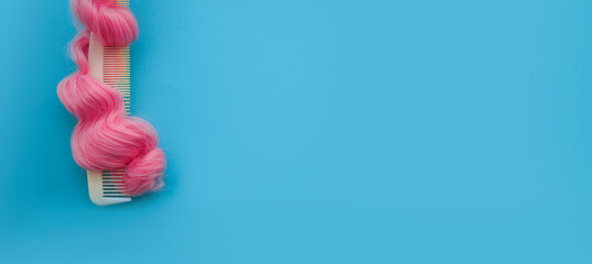 Top view on the comb in curls of bright pink hair. On a bright blue background. Banner with a copy...