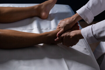 Um profissional fazendo massagem terapêutica no pé paciente que está deitado em uma maca.