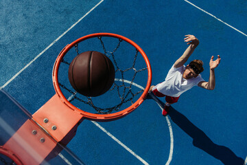 top view of ball in basketball ring and young man training on court