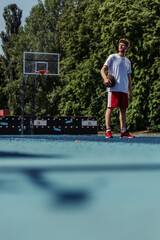 full length of basketball player in sportswear standing with ball on modern court