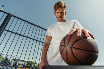 low angle view of confident basketball player looking at camera near blurred ball