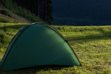 A green tent stands on a green hillock in the Alps