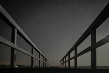 Low-angle grayscale of a fenced pathway under the starry night sky - Powered by Adobe