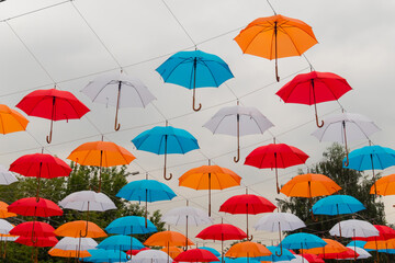 Fototapeta na wymiar Low angle view: colorful umbrellas hanging against gray overcast sky and swaying in wind at summer city festival. Street decoration, celebration, art, holiday concept