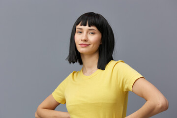 Obraz premium joyful woman with dark hair and a beautiful hairstyle looks at the camera smiling and keeps her hands on her belt. Horizontal photo with an empty space on the background for inserting an advertising 