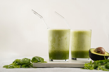 A glass of green healthy detox smoothie with spinach, matcha powder and a glass straw, fresh...