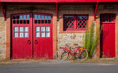 Vieux vélo rouge au pieds d'une ancienne maison en pierre en France.