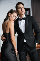 Elegant man in suit hugging brunette girlfriend in dress at home