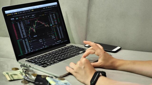 Laptop and phone to buy bitcoin on the Binance crypto exchange during the market crash. Trading, spot, staking. Workspace freelance, woman hands on keyboard 