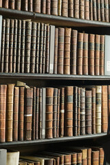 A pattern of old books on wooden shelves with natural light. Ideal for background texture