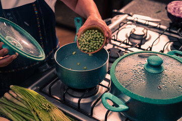 Hands putting peas in a pot of boiling water. A person using the stove at home to prepare food.