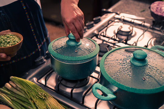 Manos quitando la tapadera de una olla con agua caliente para cocinar algunas arvejas frescas. Person cooking.