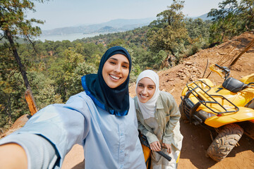 Smiling female friends looking at camera while standing near quad bike © Faces of Travel