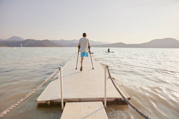 Naklejka premium Back view of disabled man walking on pier in lake