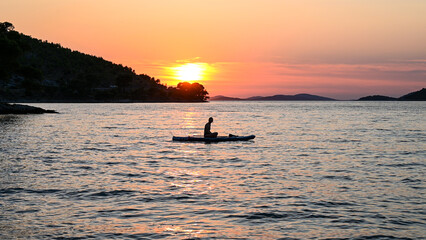 Silhouette of woman sitting on stand up paddle board on the sea. Woman enjoying on Paddle-board at summer. SUP