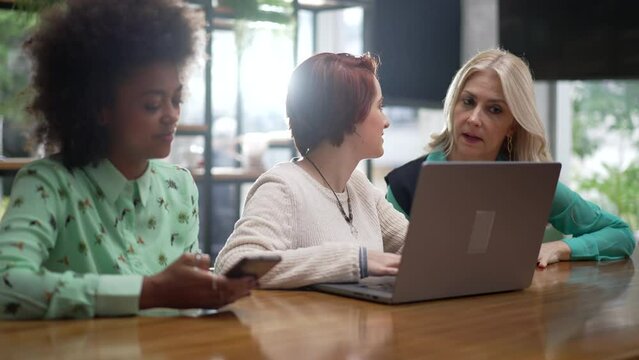 Three diverse women in front of laptop seated at coffee shop. Young employees with business woman executive coaching employees