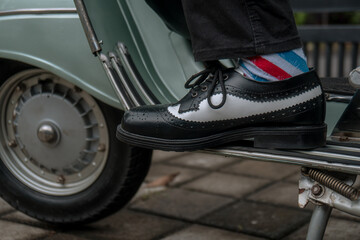 Obraz na płótnie Canvas These hand-made black-and-white wingtip shoes with loafers sole made from genuine leather are being worn to hang out with an old green Vespa
