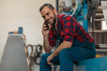 A young serviceman on work breaks sits on a machine and talks on the phone.